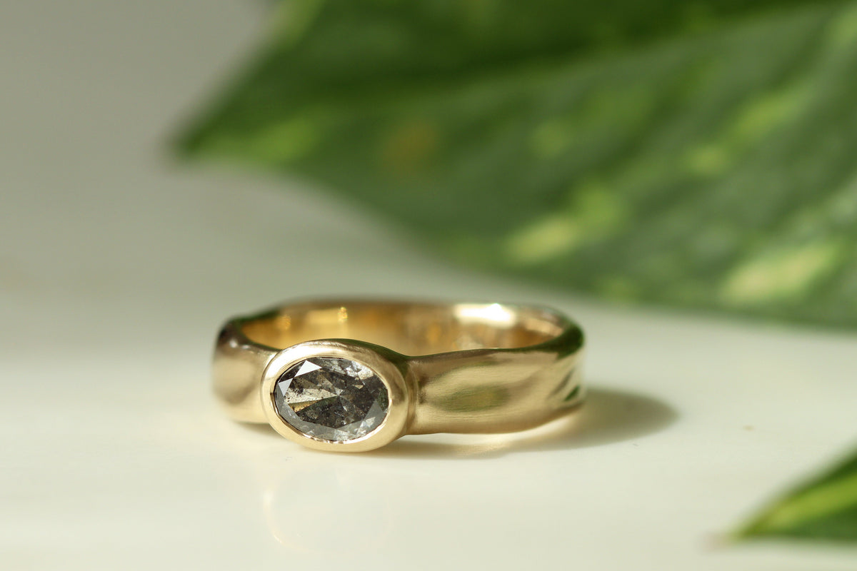 gold organic melty wavy band with bezel set salt and pepper oval diamond.
